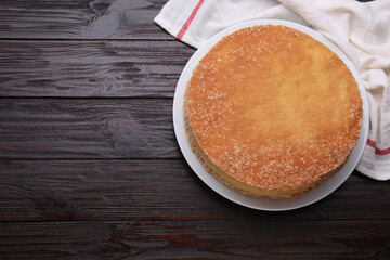 Plate with delicious sponge cake on dark wooden table, top view. Space for text