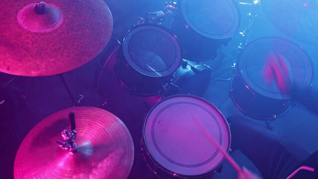 A drummer plays on a dark stage in the fog and neon lights.