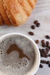 Coffee to go. Paper cup with tasty drink, croissant and beans on white wooden table, flat lay