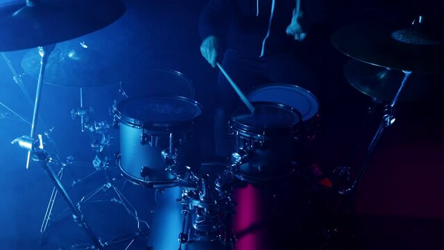 A drummer plays on a dark stage in the fog and neon lights.