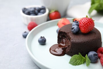 Plate with delicious chocolate fondant, berries and mint on grey table, closeup. Space for text