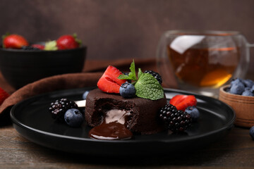 Plate with delicious chocolate fondant, berries and mint on wooden table, closeup