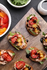 Delicious bruschettas with balsamic vinegar, tomatoes, arugula and tuna on dark textured table, flat lay