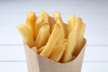 Delicious french fries in paper box on light background, closeup