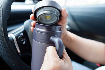 Asian woman driver hold thermo mug with hot coffee in car, dangerous and risk an accident.