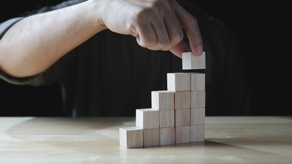 Business development to success. Businessman hand stacking wood block as step stair, business growth success on dark background. Concept of Business growth, Financial planning, Investment, Strategy