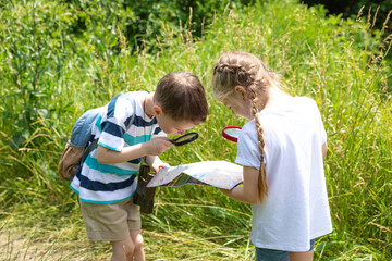 Two little children boy and girl brother and sister with magnifying glass and map while exploring forest nature and environment on sunny day during outdoor ecology