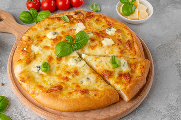 Pizza four cheeses with fresh basil on top on a wooden board on a gray concrete background. Top view, copy space.