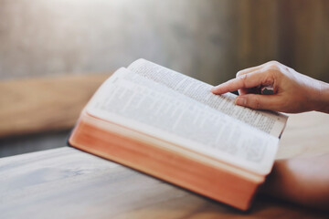 Close up of a woman hand  hold and pointing  the open bible, blurred page on wooden table with window light and Bokeh, Christian devotional, spiritual or bible study concept background with copy space
