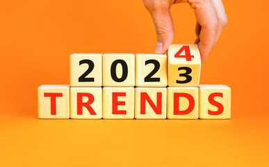 2024 trends new year symbol. Businessman turns a wooden cube and changes words Trends 2023 to Trends 2024. Beautiful orange table orange background, copy space. Business 2024 trends new year concept.