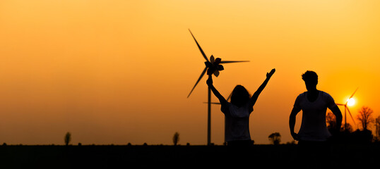 silhouette Hispanic brazillian couple standing together in front of wind turbine. Wind turbines for...
