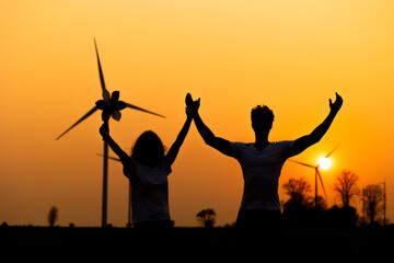 Fototapeta na wymiar silhouette Hispanic brazillian couple standing together in front of wind turbine. Wind turbines for electric power and energy. Sustainable electricity production. Happy sucess hand up