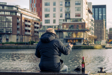 Elderly man from behind with a dark jacket and light hair with a bottle of red wine next to him...