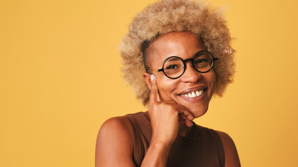 Close up, happy friendly girl in glasses, wearing brown top playfully flirting smiling looking at camera isolated on orange background, studio shot