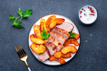 Baked pork tenderloin with sweet quince or apple slices served on white plate. Black table background, top view