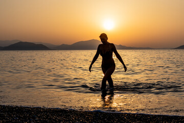 Silhouette of a woman stepping out of the sea or ocean at sunset.