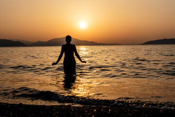 Silhouette of a woman entering the sea or ocean at sunset.