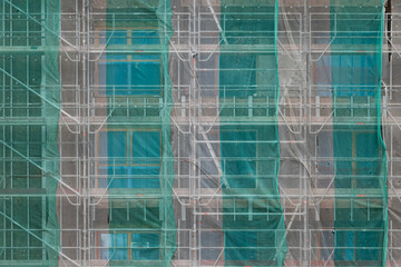 Building under construction covered in scaffolding with protective textile sheets - obrazy, fototapety, plakaty