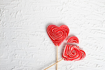 Red lollipop on a stick in the form of a heart on a white background. The concept of love and sweets. Flat layout, top view, copy space. Valentine's card. 14 of February