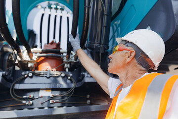 Driver mechanic checks hydraulic hoses of excavator. Man in hard hat industrial worker