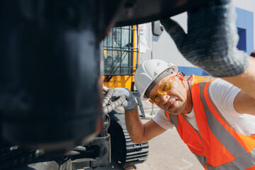 Obraz na płótnie Canvas Man in hard hat industrial worker Machinery tractor mechanic checks hydraulic hose system equipment on excavator