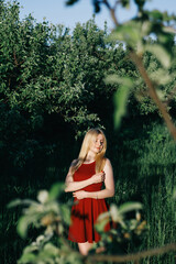 Lovely woman in red dress in the garden at sunset time.