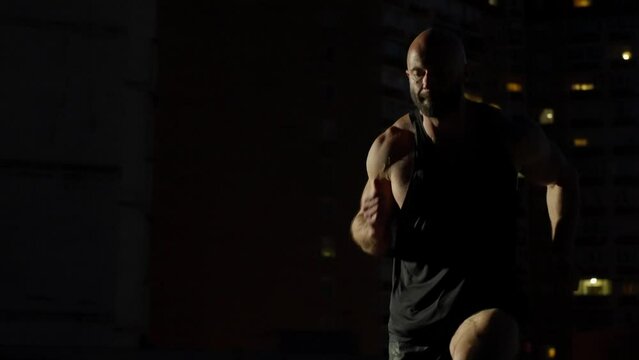 Close-up of an athlete running in one place in a night city. Circular movement of the camera around a sports man working out. High quality 4k footage