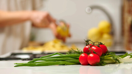Close up view of woman in white shirt peeling a potato. Peel falling onto cutting board. Lady preparing potatoes to be cut and added to stock pot for dinner.