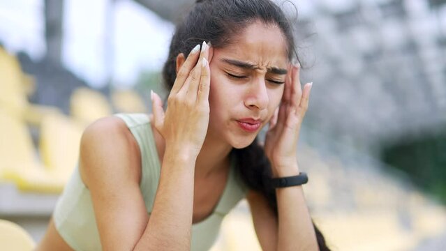 Young athletic woman feels a headache while sitting in an urban city stadium closeup. Sad female suffering from migraine or high blood pressure. She is not feeling well Close up Healthcare concept