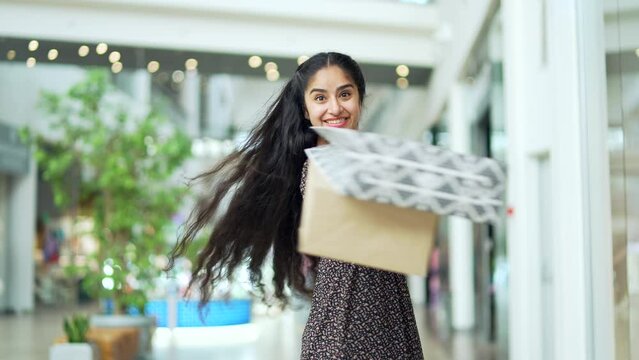 Portrait happy glad young indian woman shopping in mall after sales and discounts looking at camera joyful smiling with colorful gift bags with purchases satisfied contented content buyer lady indoors