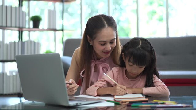 Happy Asian woman and her daughter staying together in living room, mother let her daughter learning or studying in the internet. 