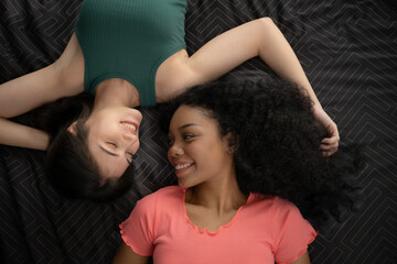 Top view of two young women lying on bed and smiling at each other