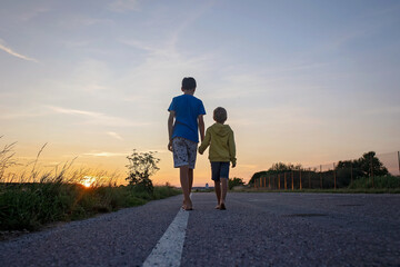 Two boys, brothers, children, blond boys with pet dog, maltese breed, walking on a road in rural, sunny day, sky