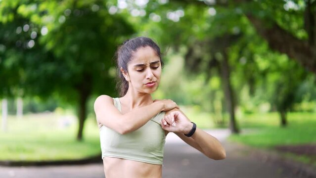 Young athletic woman sharp pain in her shoulder during a morning jog workout in urban city park. A sad female girl was injured. Unfortunate athlete rubs and massages the muscles on the sore sport