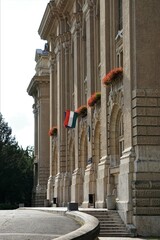 Węgierska flaga powiewa na Uniwersytecie w Debreczynie. Na budynku widać liczne zdobienia i czerwone kwiaty. - obrazy, fototapety, plakaty