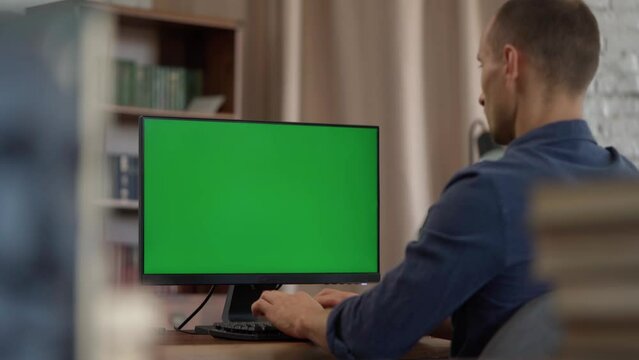 Young Man Working at His Desk Using Computer with Green Mock-up Screen, Chroma Key Display. Working from Cozy Home Office, Studio