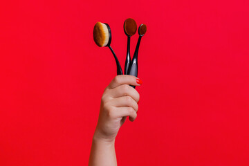 Makeup brushes in woman hand on the red background. Makeup brushes set.