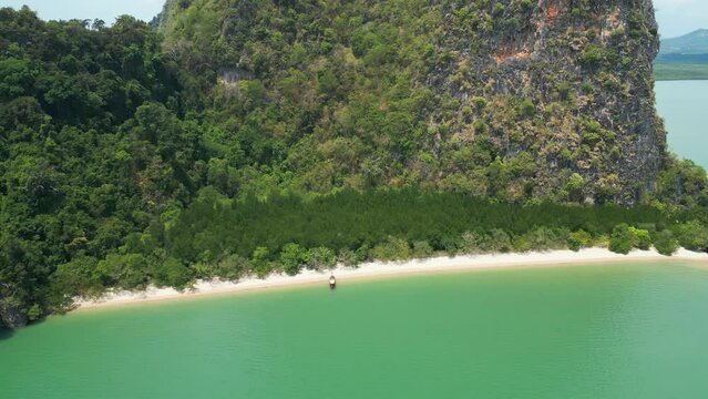 Paradise sea sand beach coastline Asian moored longtail boat. Aerial view mountain greenery lush vegetation drone shot high natural cliff rock travel shore coast harbor water transport rasta roof 4k