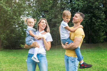 Obraz premium Family with children in the park. Mom, dad, son and little daughter in jeans and white t-shirts laugh and hug. Love and tenderness.