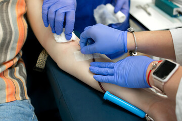 blood donation, two nurses in blue gloves connect the collection system with a needle to the...