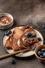 Chocolate crepes with blueberry and chocolate paste on brown textured background rustic style