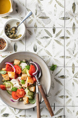Traditional italian panzanella with mozzarella, tomatoes, capers, onion, croutons, cucumbers. Summer salad served on printed tile background with copy space top view