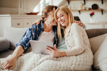 Mature couple using a tablet while sitting on the couch in the living room at home