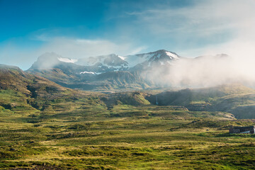 View of rural scene with fog covered mountain and tiny waterfall in summer at Iceland