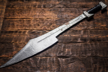 Ancient Spartan sword on the wooden table background concept. Top view.