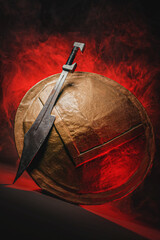 Ancient Spartan sword and shield on the dark background in the red light smoke concept.