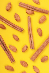 Almonds and cinnamon sticks on a yellow background.