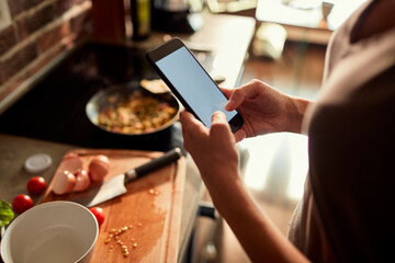 Young woman using a smart phone while cooking and preparing a healthy meal