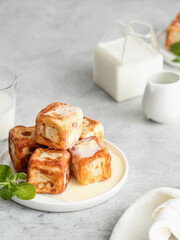 Cottage cheese pancakes in the form of cubes with condensed milk or cream sauce and mint leaves on gray background with text space