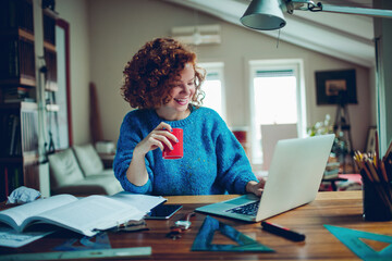 Young woman having a coffee while using a laptop and studying at home